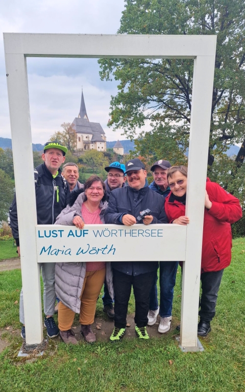 Das Foto zeigt fünf Männer und zwei Frauen, welche durch einen großen Rahmen in die Kamera lächeln. Der Rahmen trägt die Aufschrift 
