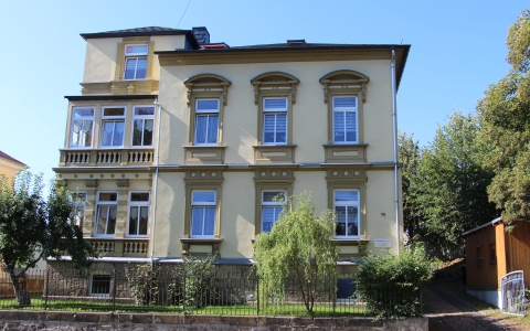 Mehrstöckiges historisches Wohnhaus mit verzierten Fensterrahmen und kleinem Vorgarten mit Bäumen und Sträuchern