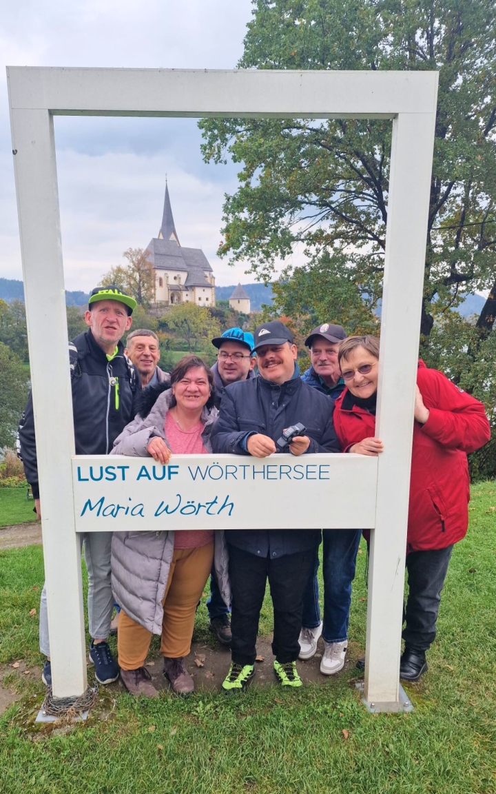 Das Foto zeigt fünf Männer und zwei Frauen, welche durch einen großen Rahmen in die Kamera lächeln. Der Rahmen trägt die Aufschrift 
