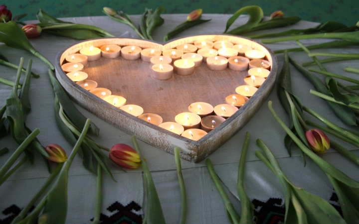 Herzförmiges Tablett mit brennenden Teelichtern umgeben von liegenden Tulpen auf einem Tuch.